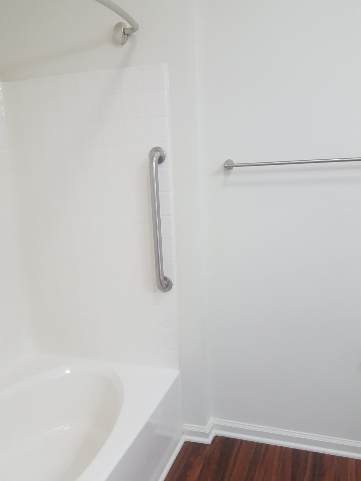 A minimalist bathroom with a bathtub, grab bar, and towel rack.