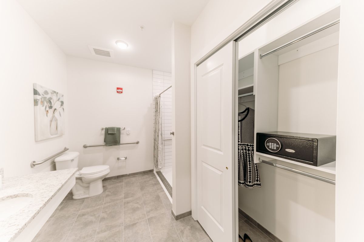 A modern, clean bathroom with a toilet, shower, and closet featuring a safe.