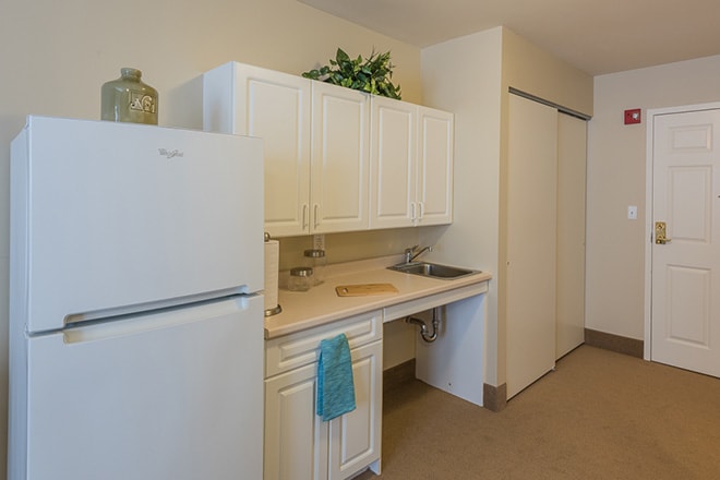 A compact kitchen area with white cabinets, a refrigerator, and a sink.