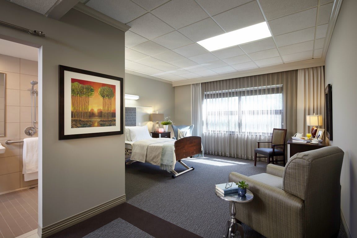 A well-lit hospital room featuring a patient bed and comfortable furnishings.