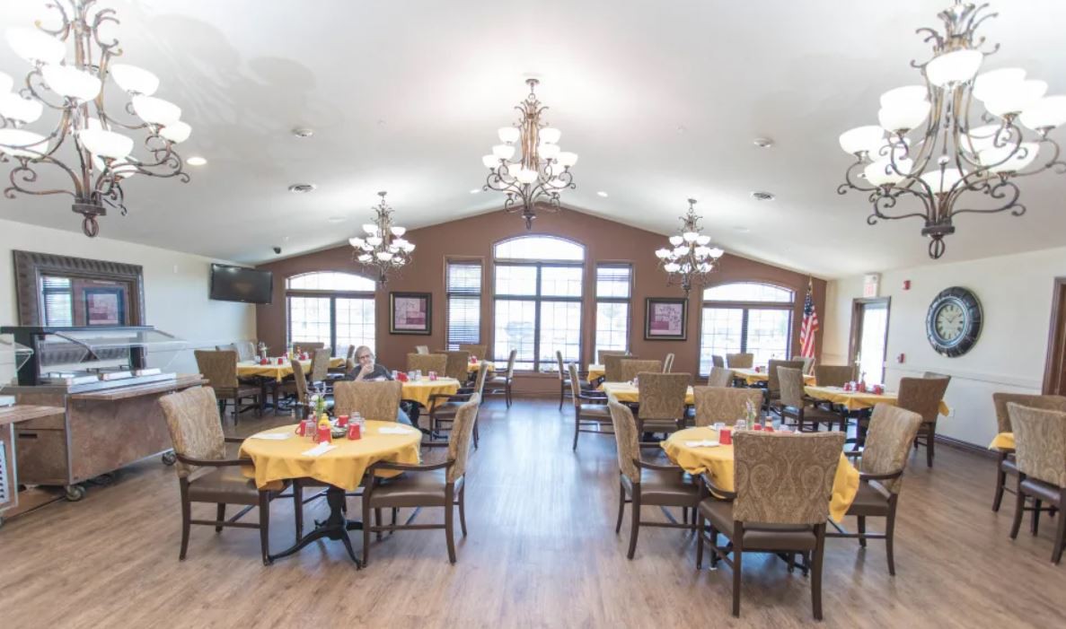 A spacious dining hall with multiple tables, chairs, and chandeliers.