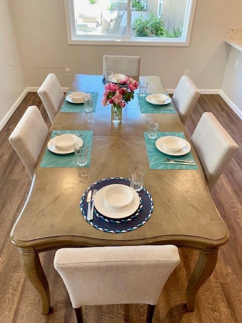 A neatly arranged dining table with a flower centerpiece and place settings for six people.