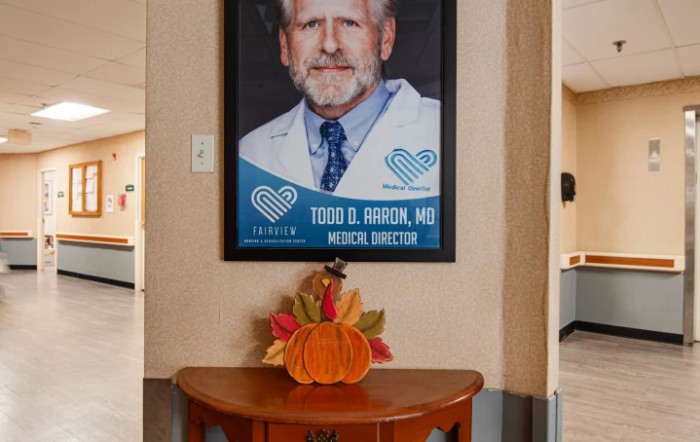 A framed portrait of a medical director displayed above a small table with an autumn-themed decoration.