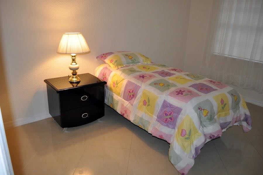 A cozy bedroom featuring a single bed with a colorful quilt, a nightstand, and a lamp.