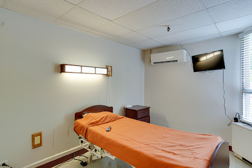 A clean and simple hospital patient room featuring an orange bedspread, air conditioning unit, and wall-mounted television.