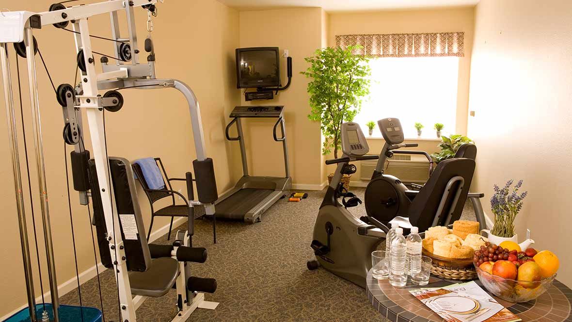 A well-equipped fitness room with various exercise machines and a TV.