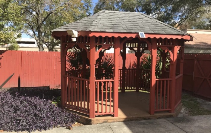 A wooden gazebo in a sunny garden setting.