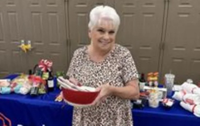 A woman smiling and holding a bowl at an indoor gathering with food in the background.