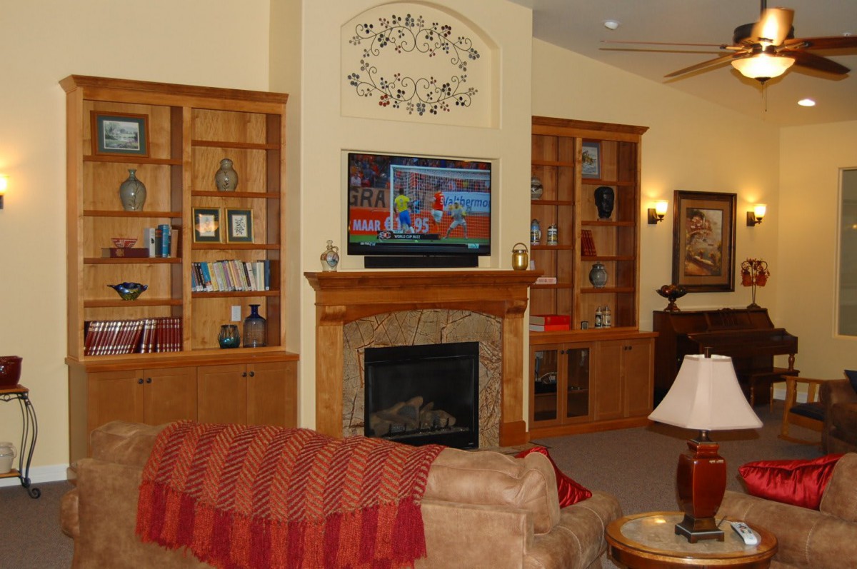 A cozy living room featuring a fireplace, built-in bookshelves, and a television mounted above the mantel.