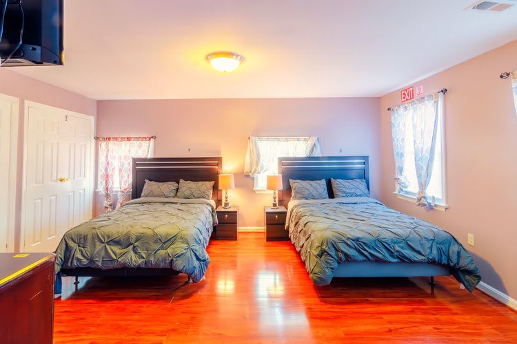 A bright bedroom with two neatly made beds and hardwood flooring.