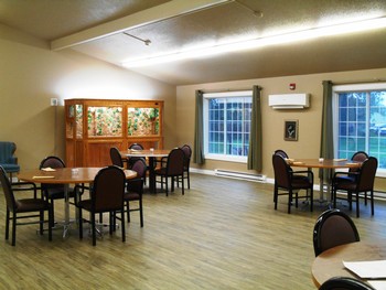An empty dining room with tables and chairs, featuring a large window and wooden flooring.
