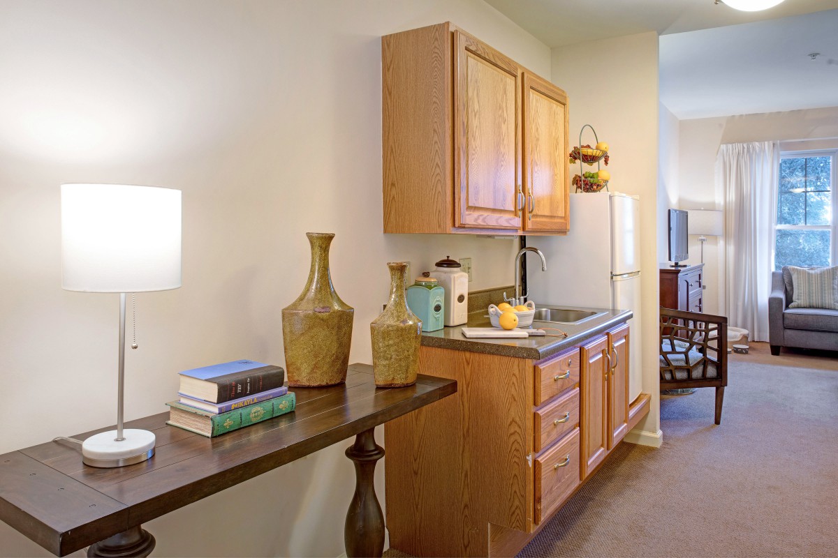 A cozy kitchen area with wooden cabinets and countertop, decorated with vases and books.