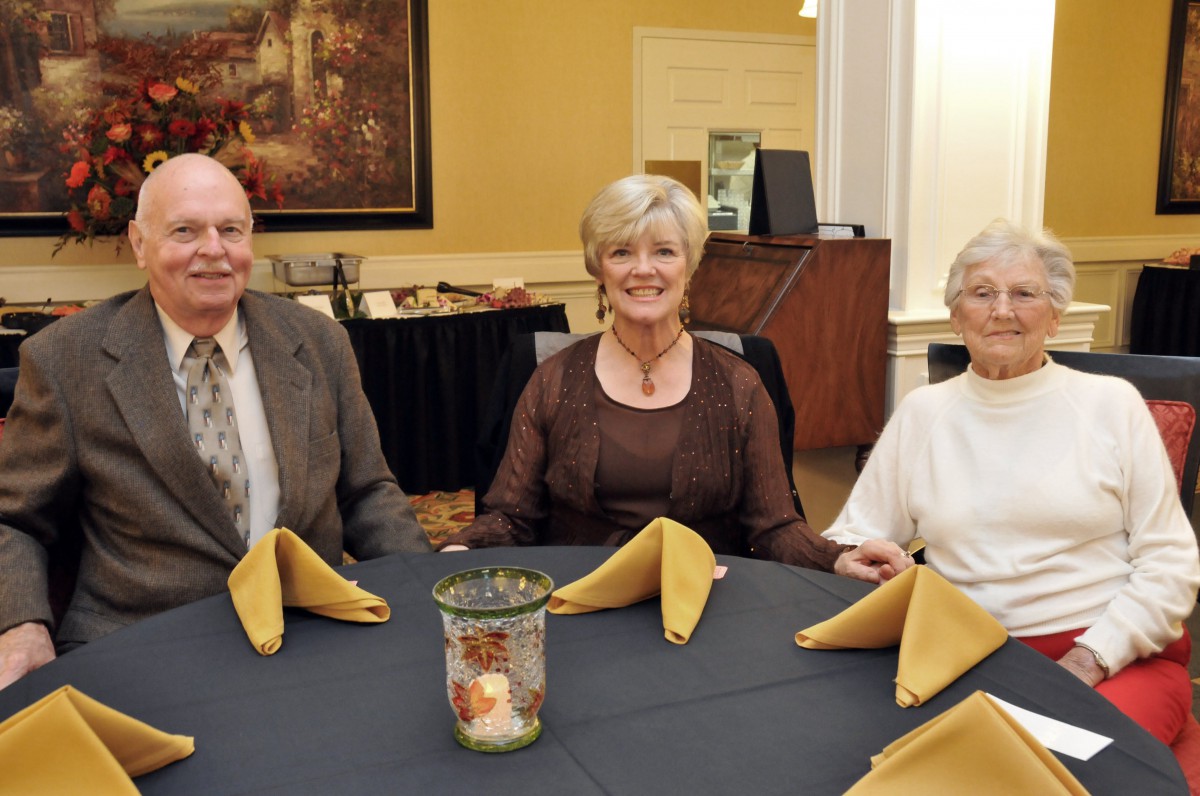 Three people sitting at a round dining table with folded napkins.