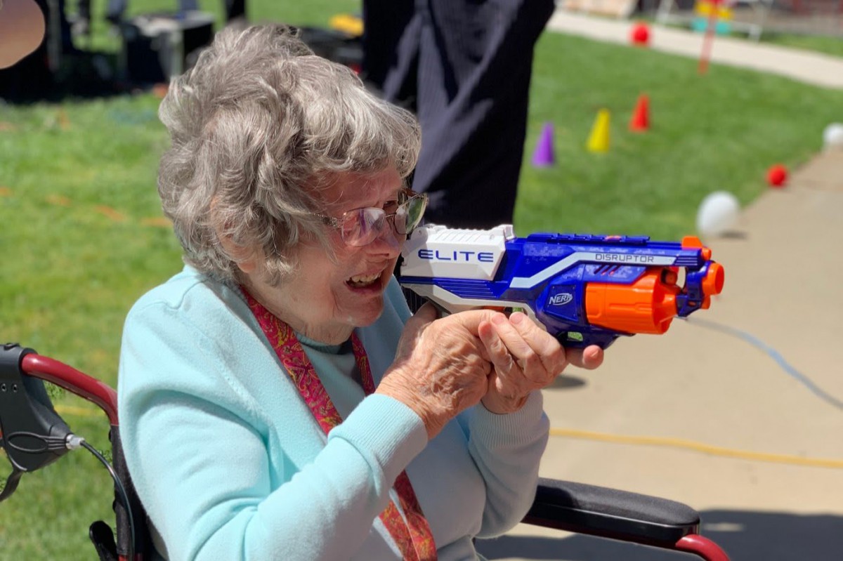 An elderly woman having fun outdoors with a water gun.