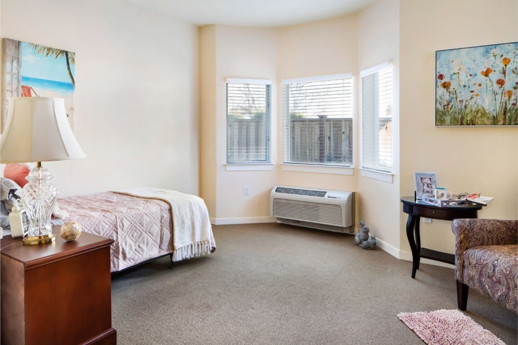A cozy bedroom with a single bed, large windows, and neutral-colored walls.
