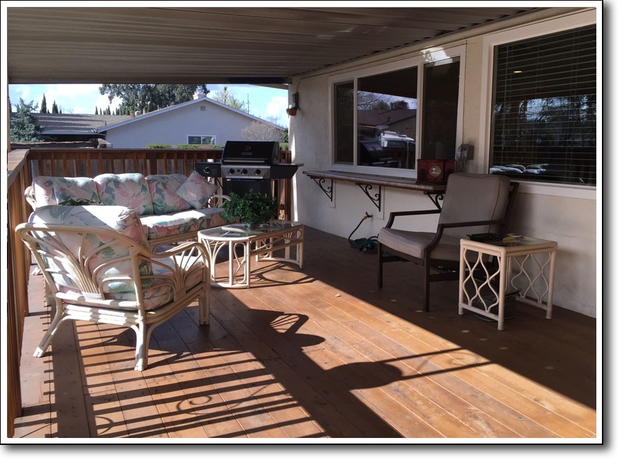 A cozy outdoor deck with patio furniture and a wooden floor, basking in sunlight.
