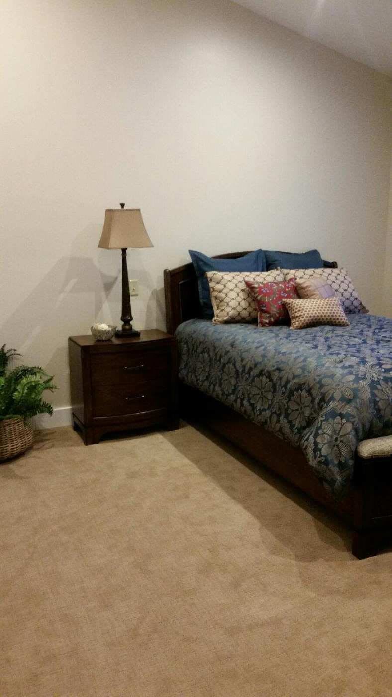 A cozy bedroom with a neatly made bed, nightstand, and decorative pillows.