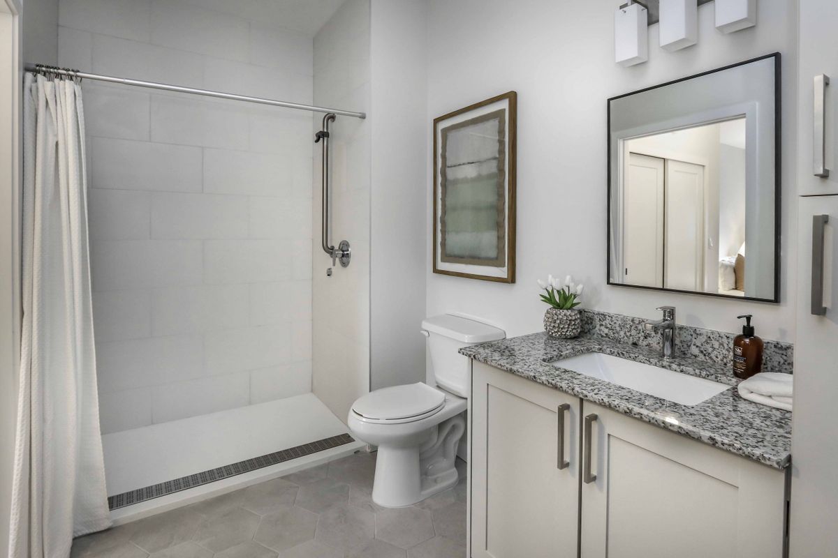 A modern bathroom featuring a shower, toilet, and granite-topped vanity with a mirror.