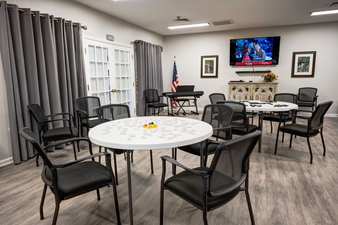An empty meeting room with round tables and chairs, a television on the wall, and an American flag in the corner.