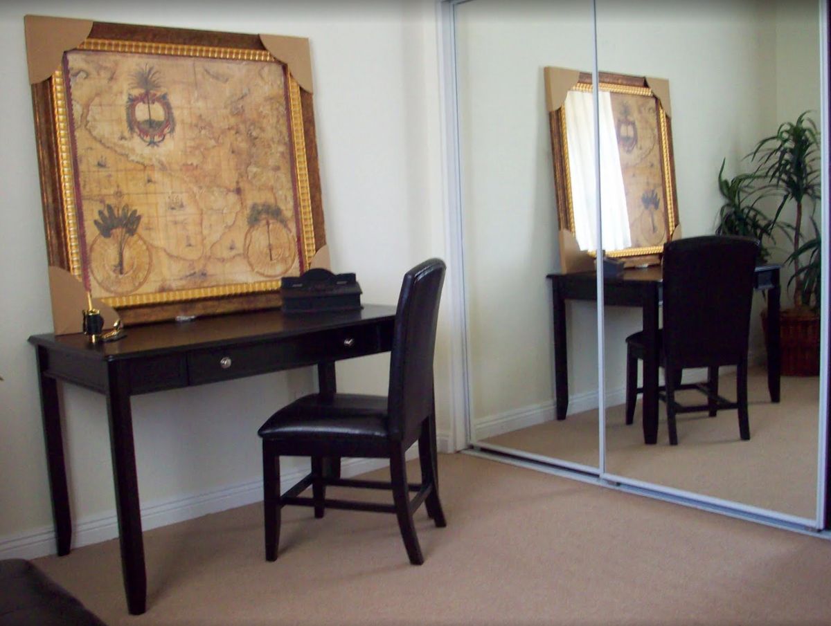 A room with a desk and chair facing a large mirrored closet, featuring a framed map on the wall.