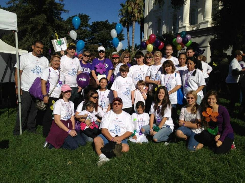 A large group of people gathered outdoors, wearing event t-shirts, with colorful balloons and a building in the background.