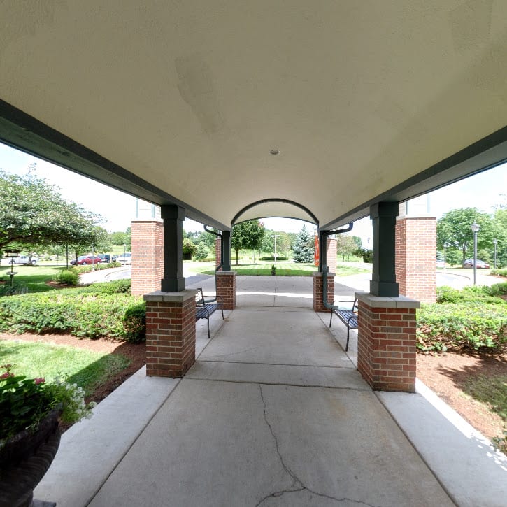 A covered walkway with brick pillars leads through a landscaped garden area.