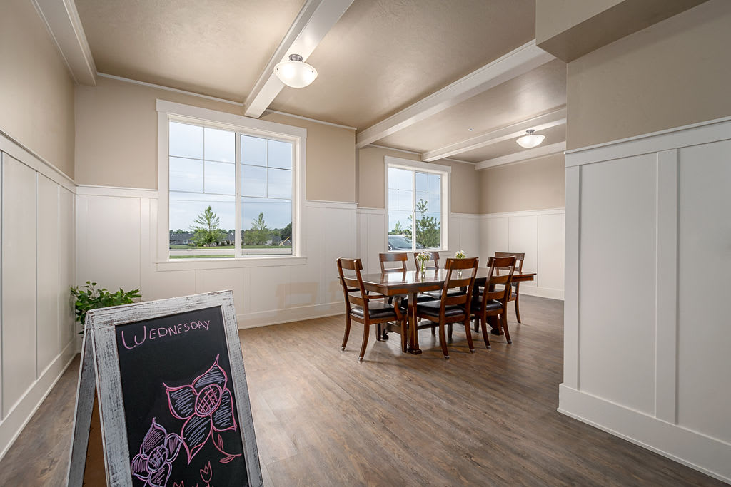 A bright dining room with a wooden table and chairs, featuring large windows and wooden flooring.