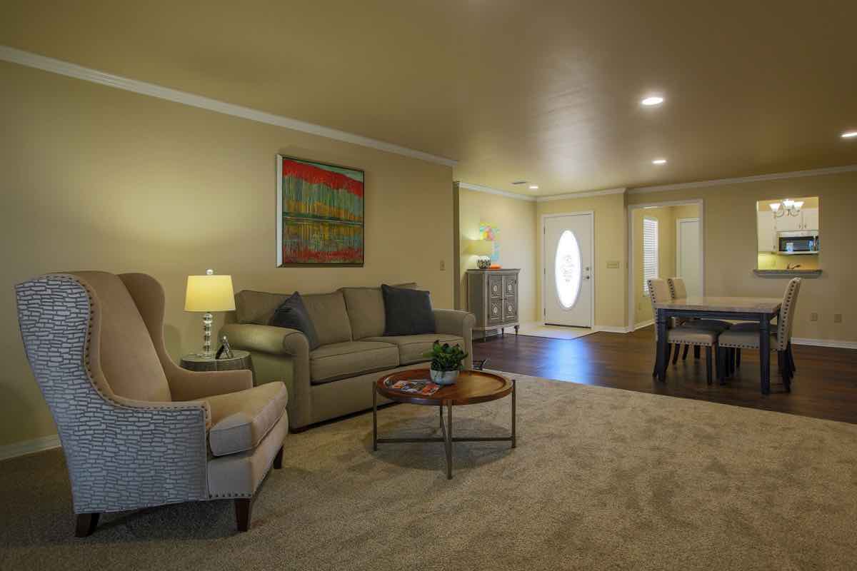 A cozy living room with a sofa, armchair, and coffee table, adjacent to a dining area.