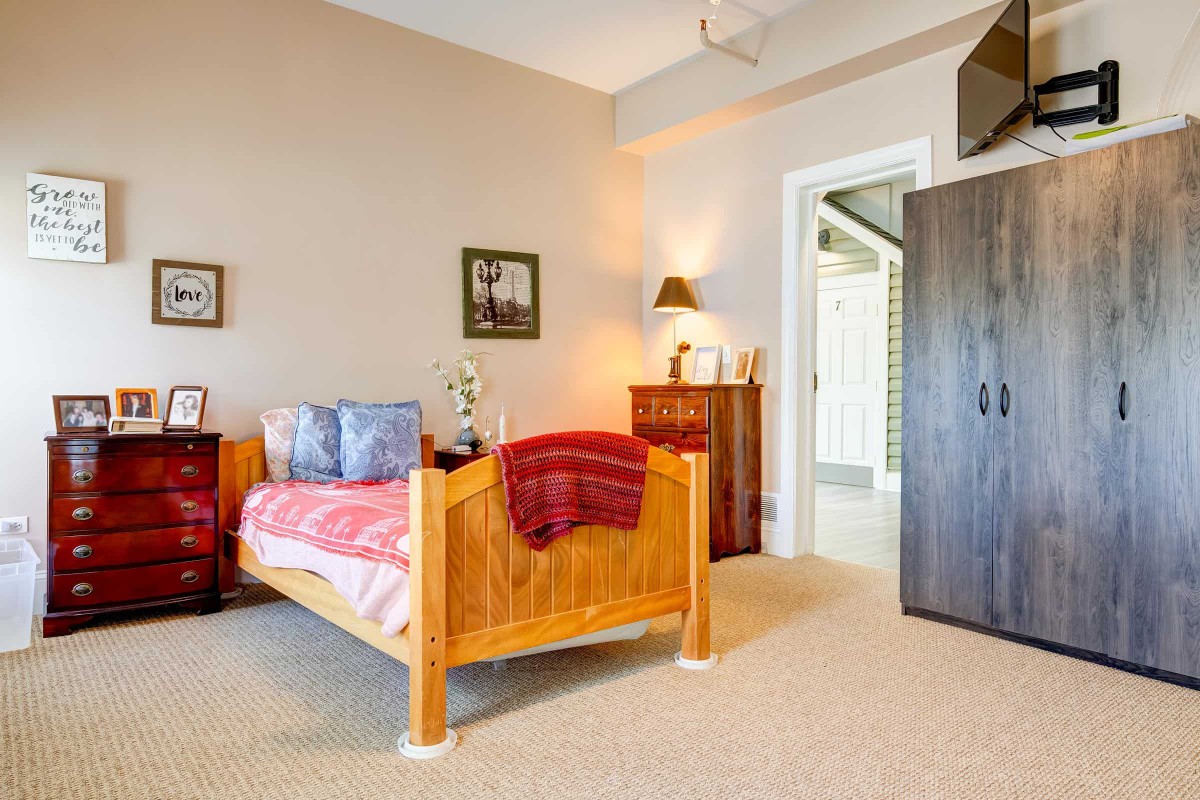 A cozy bedroom with a wooden bed, decorated with a red blanket and pillows, featuring a dresser and wall art.
