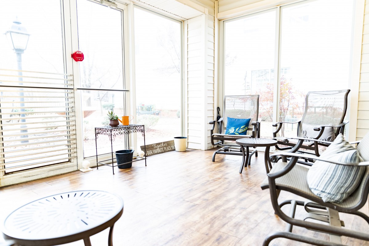 A bright sunroom filled with natural light, featuring comfortable chairs and a table.