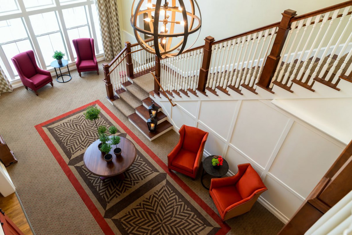 A stylish lobby features a staircase, vibrant chairs, and a decorative table under a large chandelier.