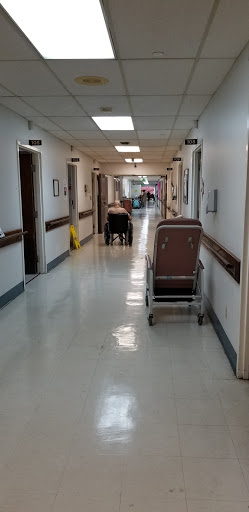 A view of a hospital hallway, featuring a wheelchair and patient transport equipment.