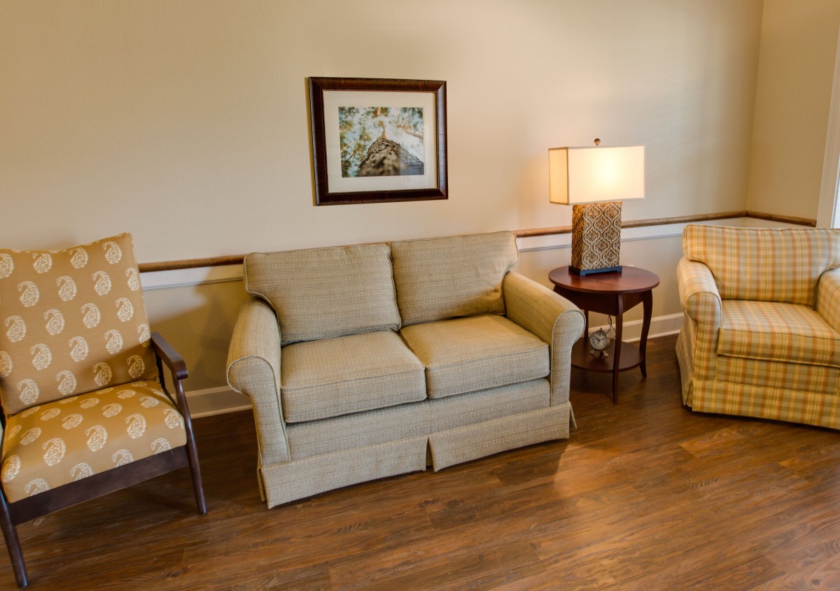 A cozy living room with a sofa, chairs, a lamp, and a painting on the wall.