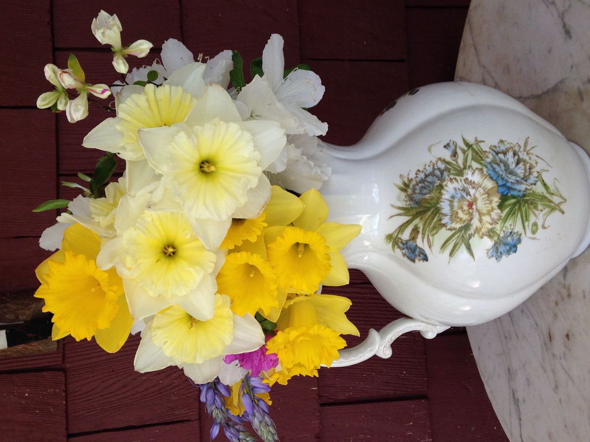 A decorative teapot filled with a bouquet of yellow and white flowers.
