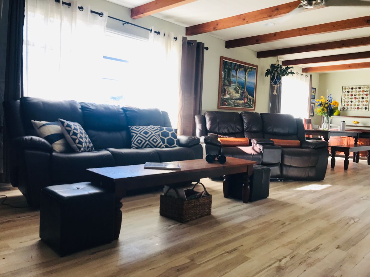 A cozy living room with sofas, a coffee table, and wooden floors, illuminated by natural light from the windows.