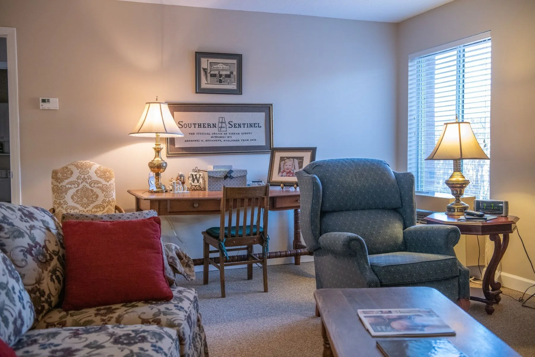 A cozy living room with a comfortable armchair and a small desk with lamps providing warm lighting.