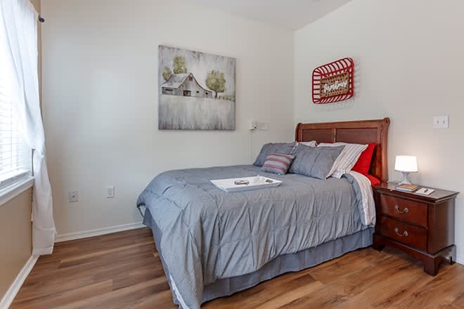 A cozy bedroom featuring a neatly made bed with gray bedding, artwork on the walls, and a wooden floor.