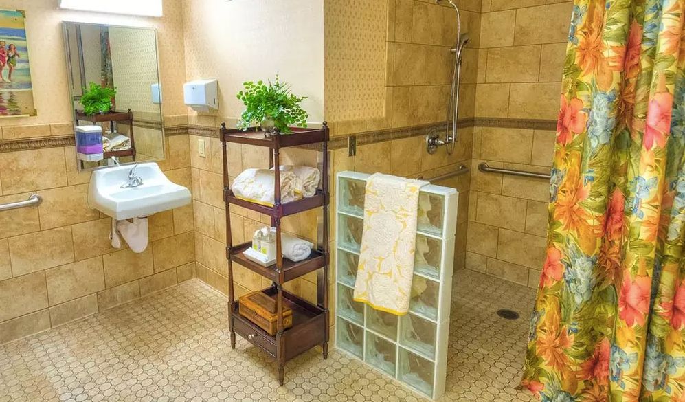 A well-organized bathroom with a wooden shelf holding towels and a plant, a tiled floor, and a walk-in shower area.