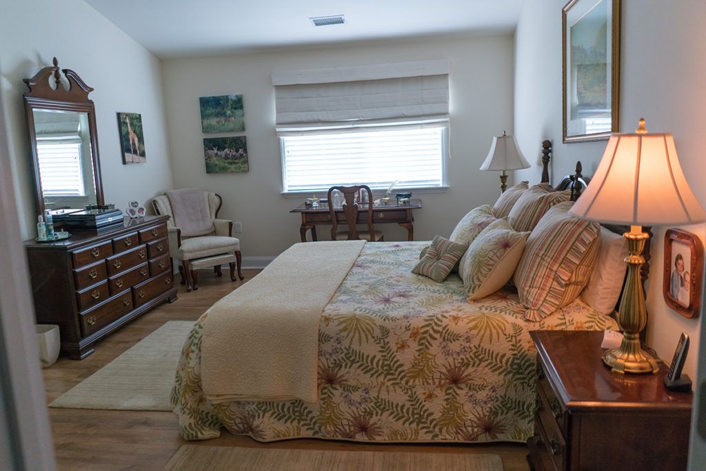 A cozy bedroom with a neatly arranged bed, decorative pillows, and classic furniture.