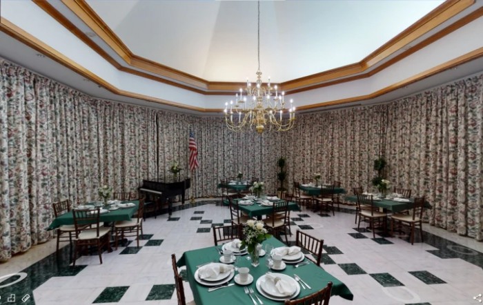 A sophisticated dining room with green tablecloths, elegant chandelier, and a piano in the corner.