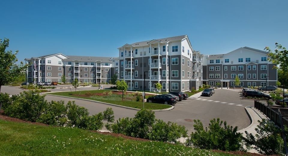 A modern apartment complex with landscaped surroundings and a parking lot under a clear blue sky.