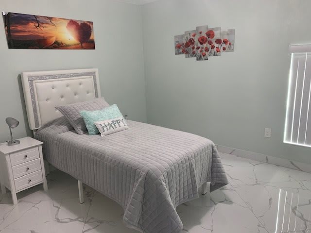 A minimalist bedroom featuring a single bed with gray bedding, accent pillows, and wall art.