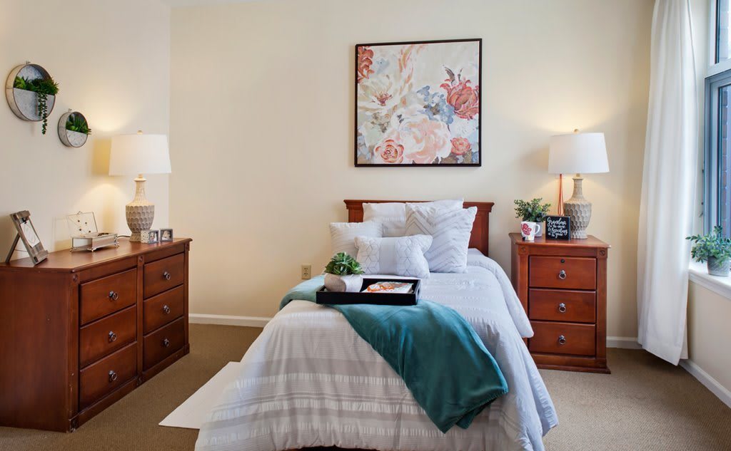 A cozy bedroom with a neatly made bed, wooden furniture, and soft lighting.