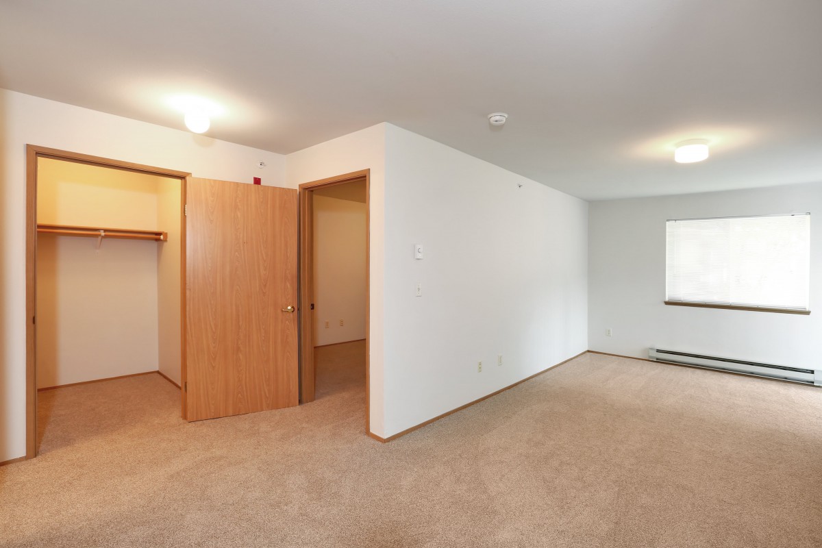 An empty bedroom with carpet flooring, a closet, and a window.