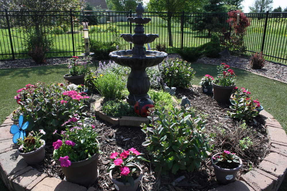 A beautifully landscaped garden featuring a decorative fountain surrounded by vibrant flowers and lush greenery.