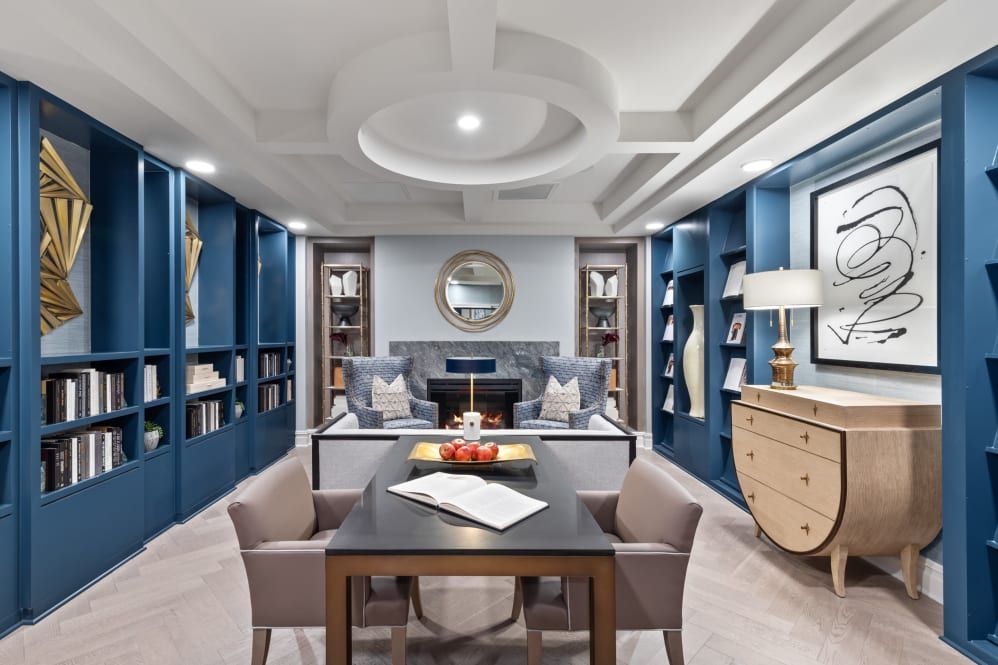 A luxurious home office with modern blue walls, elegant furniture, and built-in bookshelves.