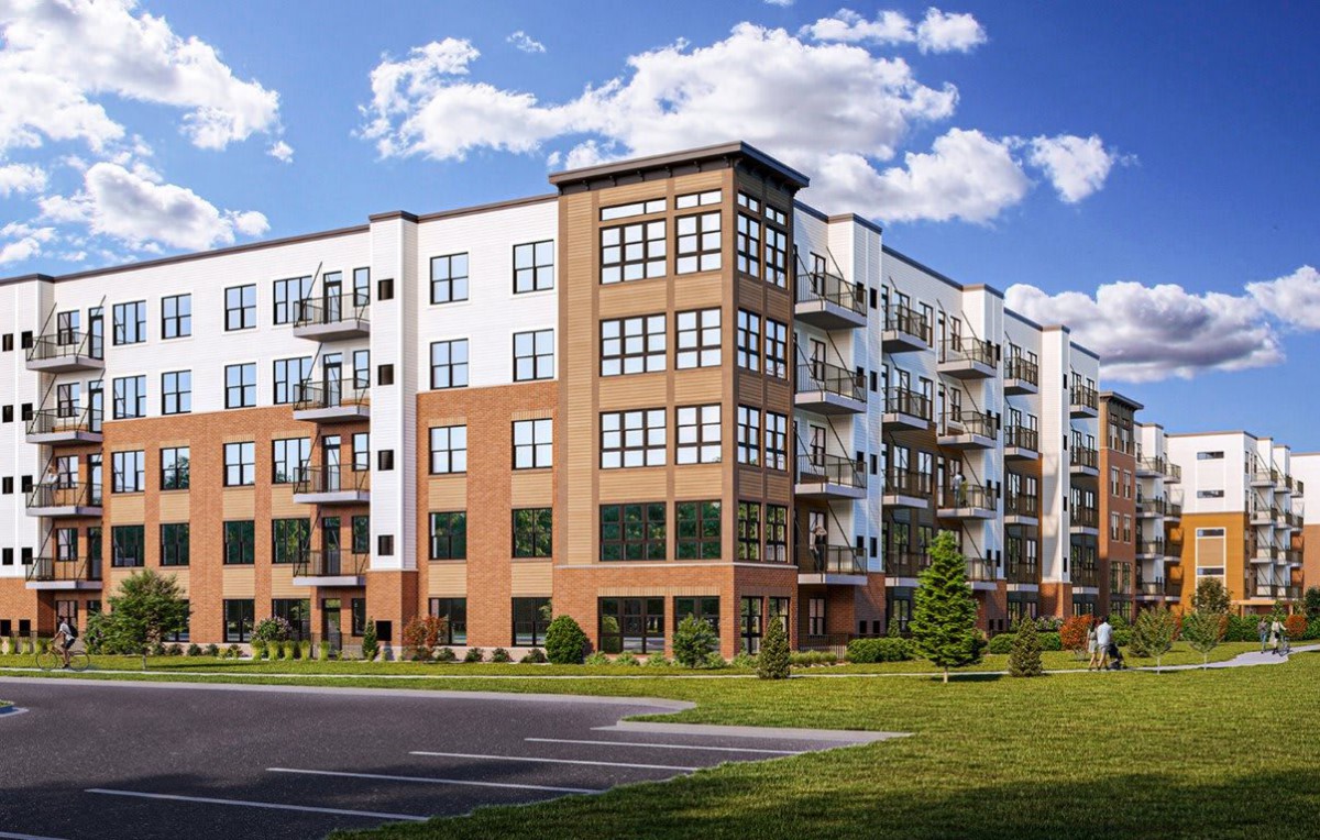A modern apartment building with brick and white exterior, featuring balconies and surrounded by green space.