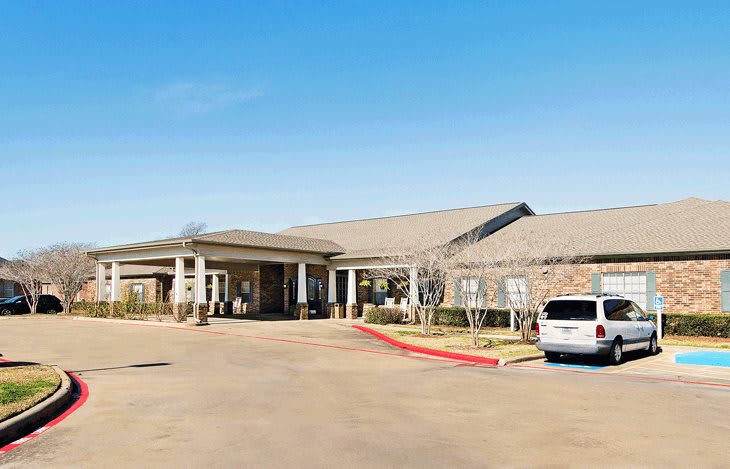A single-story building with a parking lot and a car under a clear blue sky.