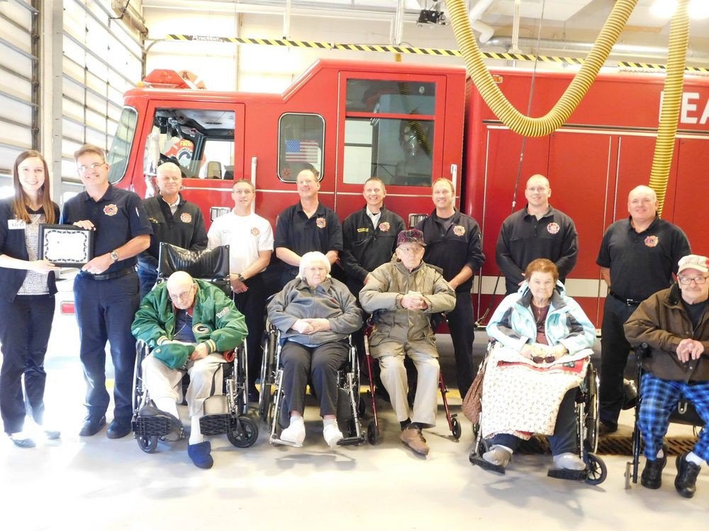 Firefighters pose with community members in wheelchairs in front of a fire truck.