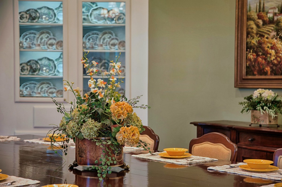 A beautifully set dining room table with a floral centerpiece and decorative china cabinet.